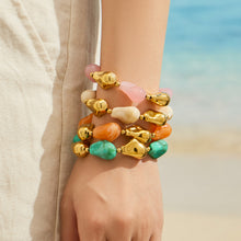 Stacked chunky resin bracelets in pink yellow green and neutral tones worn on a model wrist