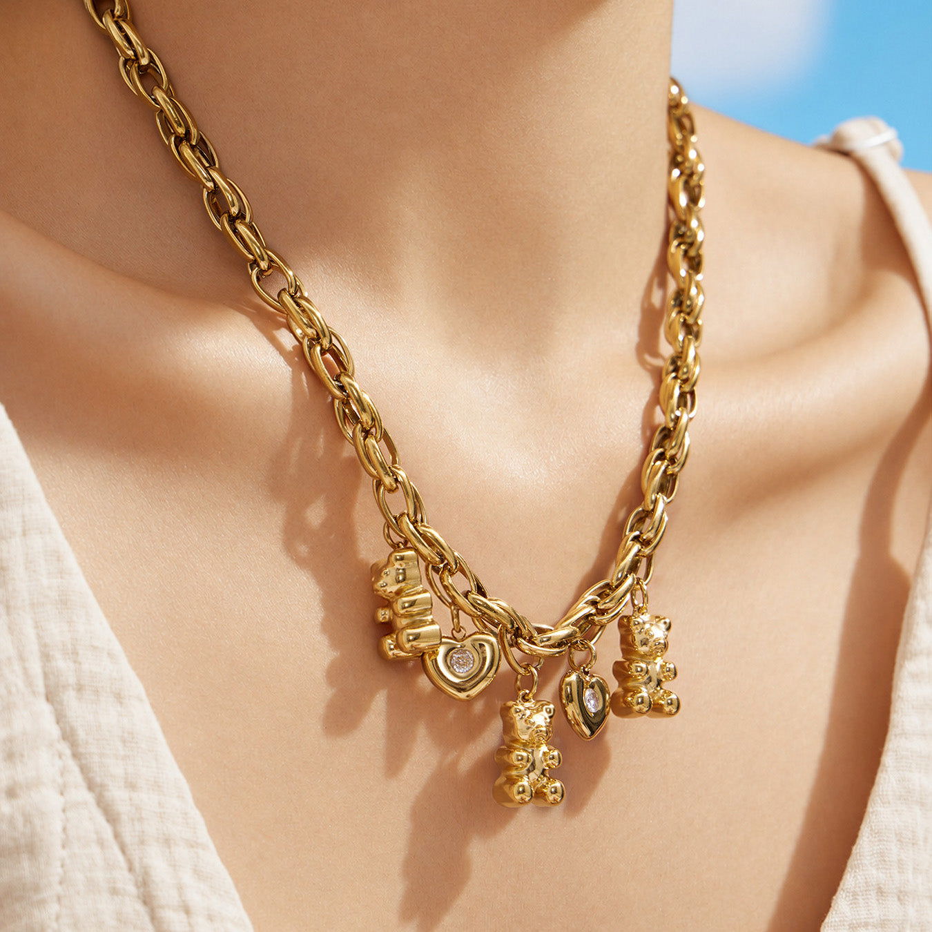 Model wearing a chunky gold teddy bear charm necklace with multiple dangling charms