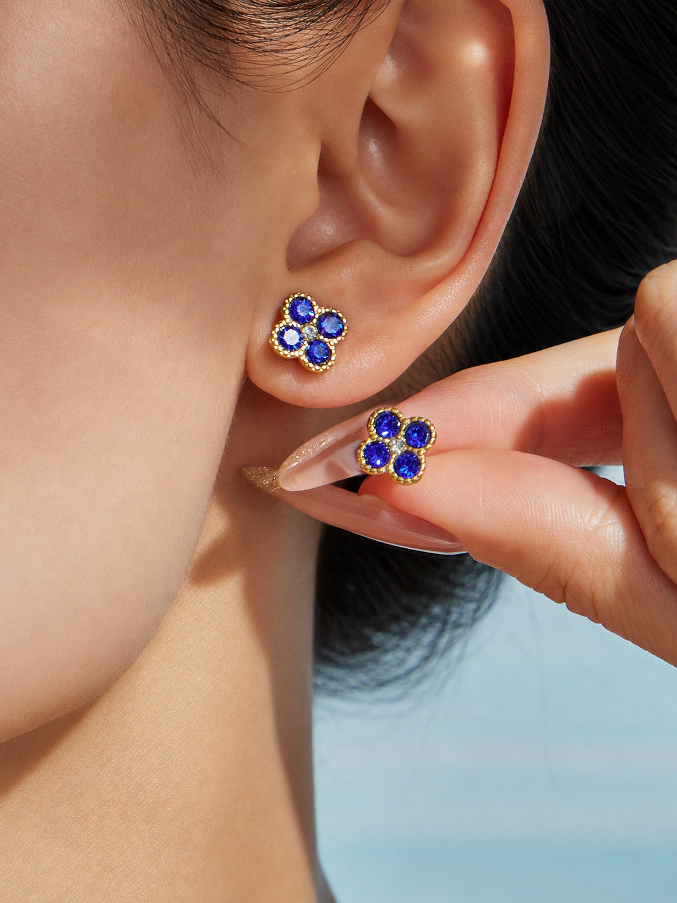 Close-up of colorful clover zircon earrings worn on ear with polished stainless steel finish