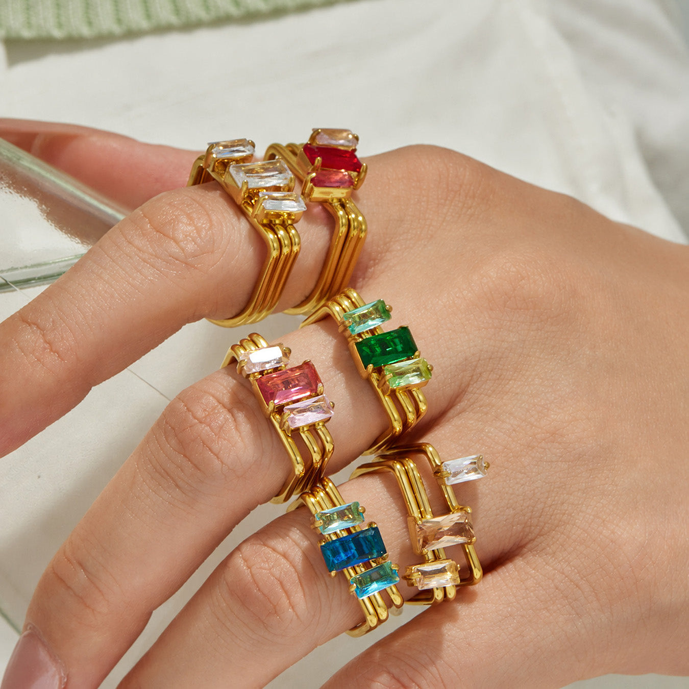 Close-up of red green blue and pink emerald-cut CZ statement rings worn together
