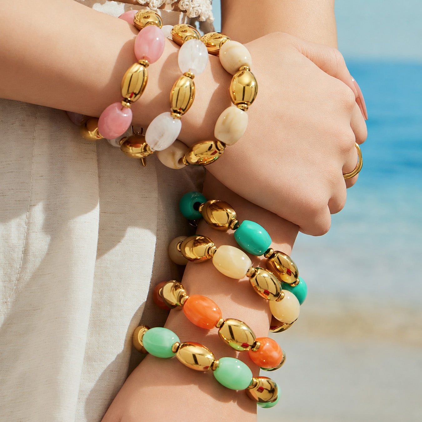 Model wearing stacked pink, white, ivory, yellow, green and orange resin bead bracelets with gold-tone accents