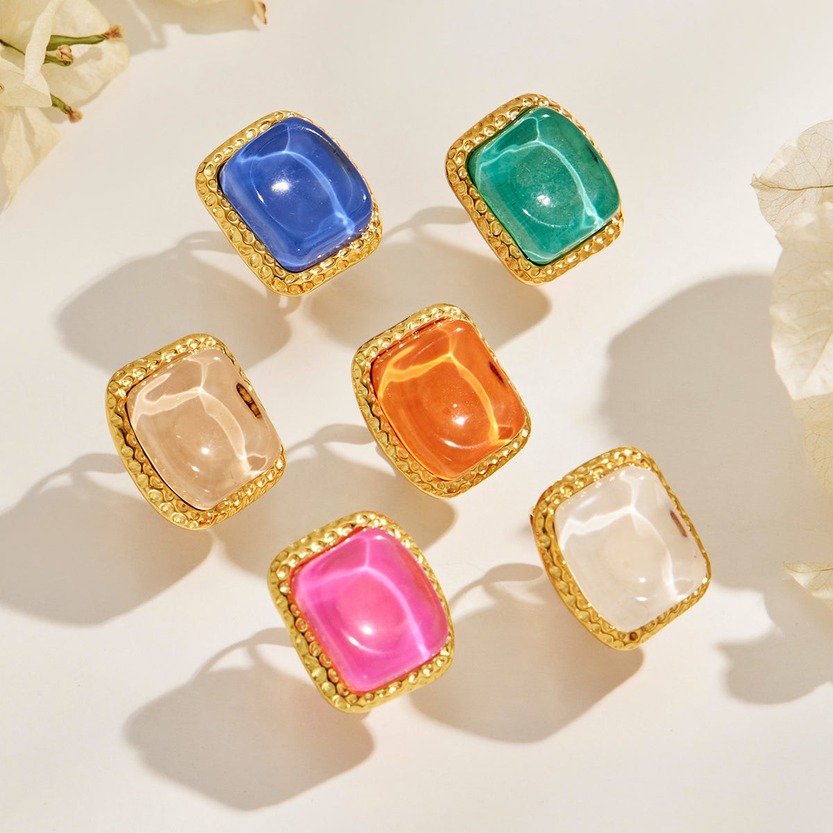 Colorful square resin rings with gold-tone textured frames in flat lay