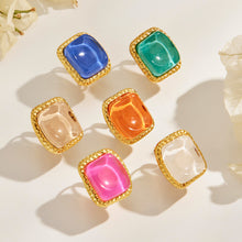 Colorful square resin rings with gold-tone textured frames in flat lay