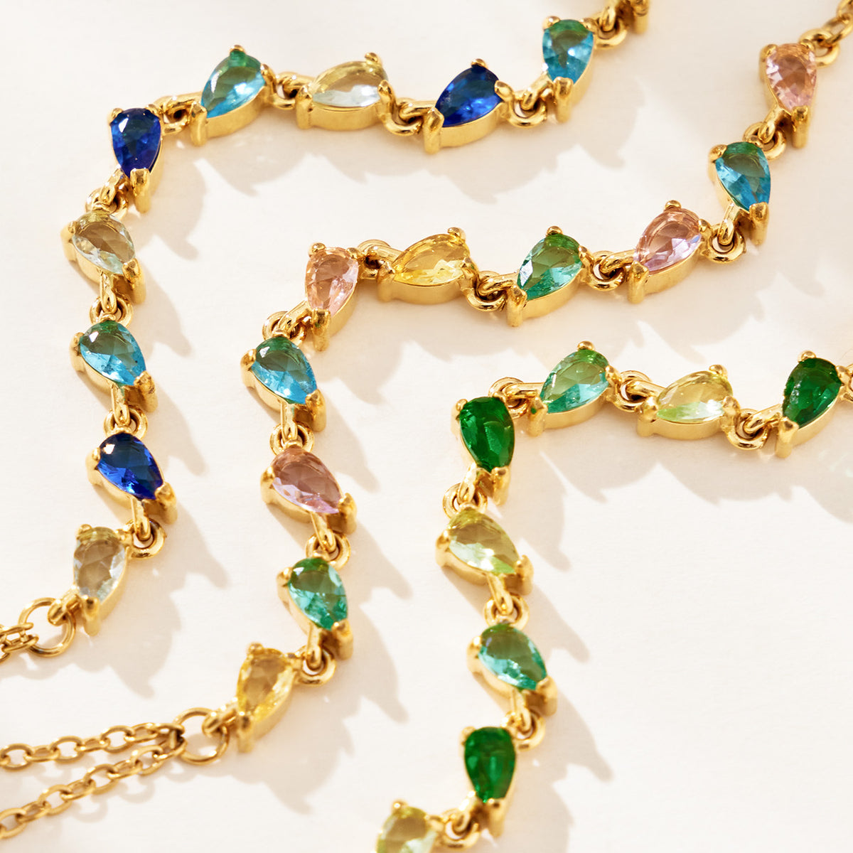 Close-up of colorful teardrop-shaped CZ stones linked along gold-tone hand chains