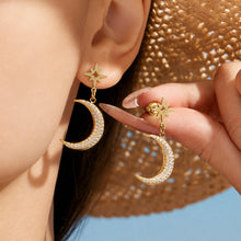 Model displaying gold crescent moon drop earrings with celestial star details