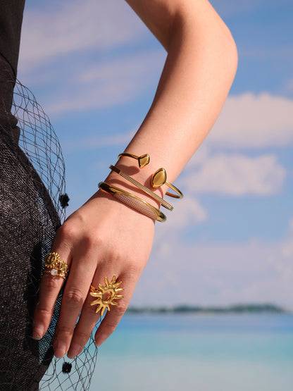crescent zircon paved bangle model lifestyle photo - stacked gold bangles on wrist with beach background