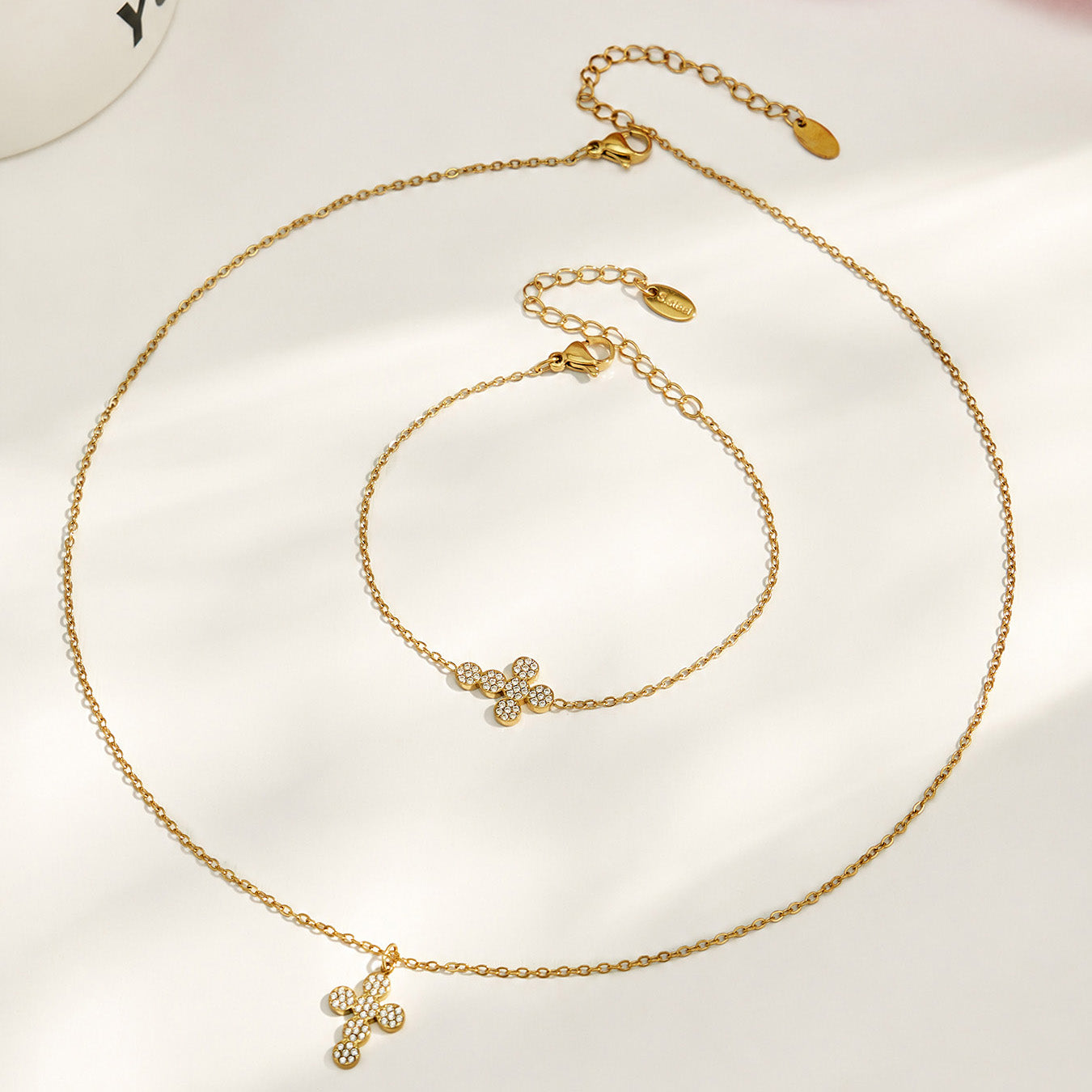 Gold cross pendant necklace and matching bracelet styles arranged in a circular display