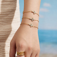 Gold cross zircon bracelet worn on the wrist against a coastal background