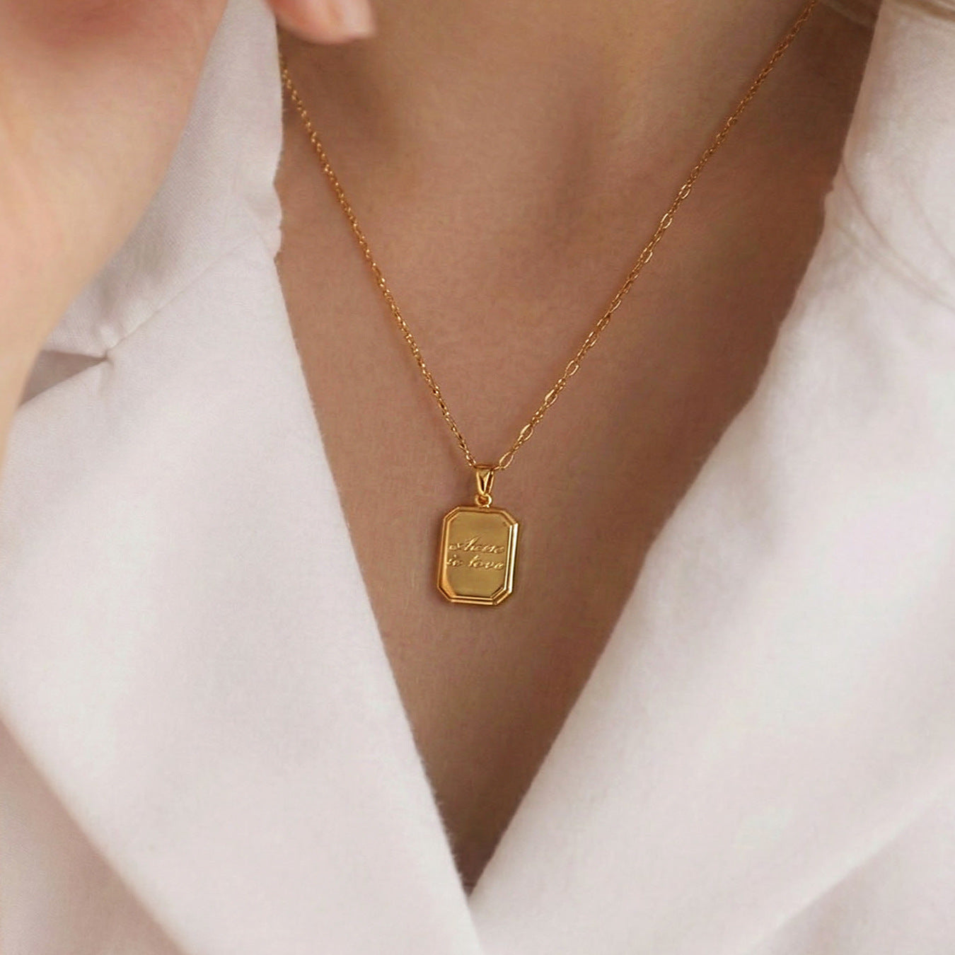 Woman wearing dainty 18K gold plated stainless steel "where is love" tag necklace with dual paperclip chain, elegant white shirt lifestyle shot