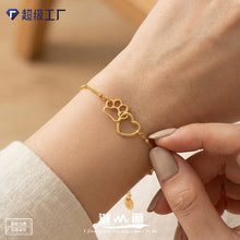 Close-up of a dainty gold paw print and heart chain bracelet worn on the wrist