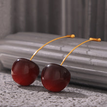 Dark burgundy resin cherry earrings displayed on a black textured stand