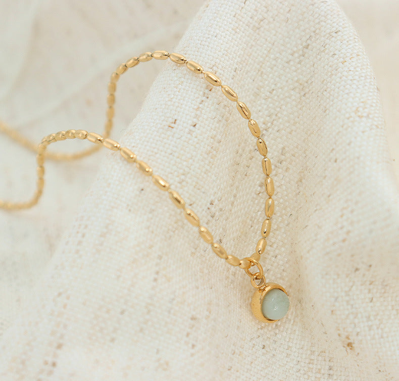 Delicate gold stainless steel necklace with round natural stone pendant arranged in a minimal flat lay