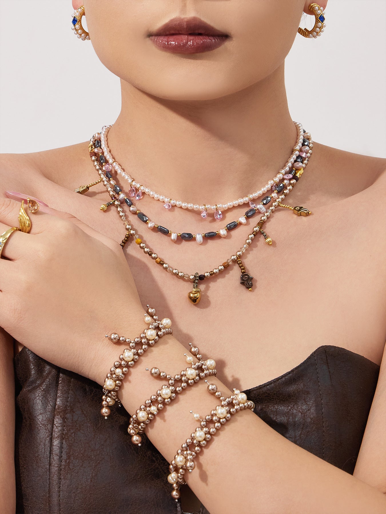 Model in a black dress wearing a double-row shell pearl bracelet and layered necklaces