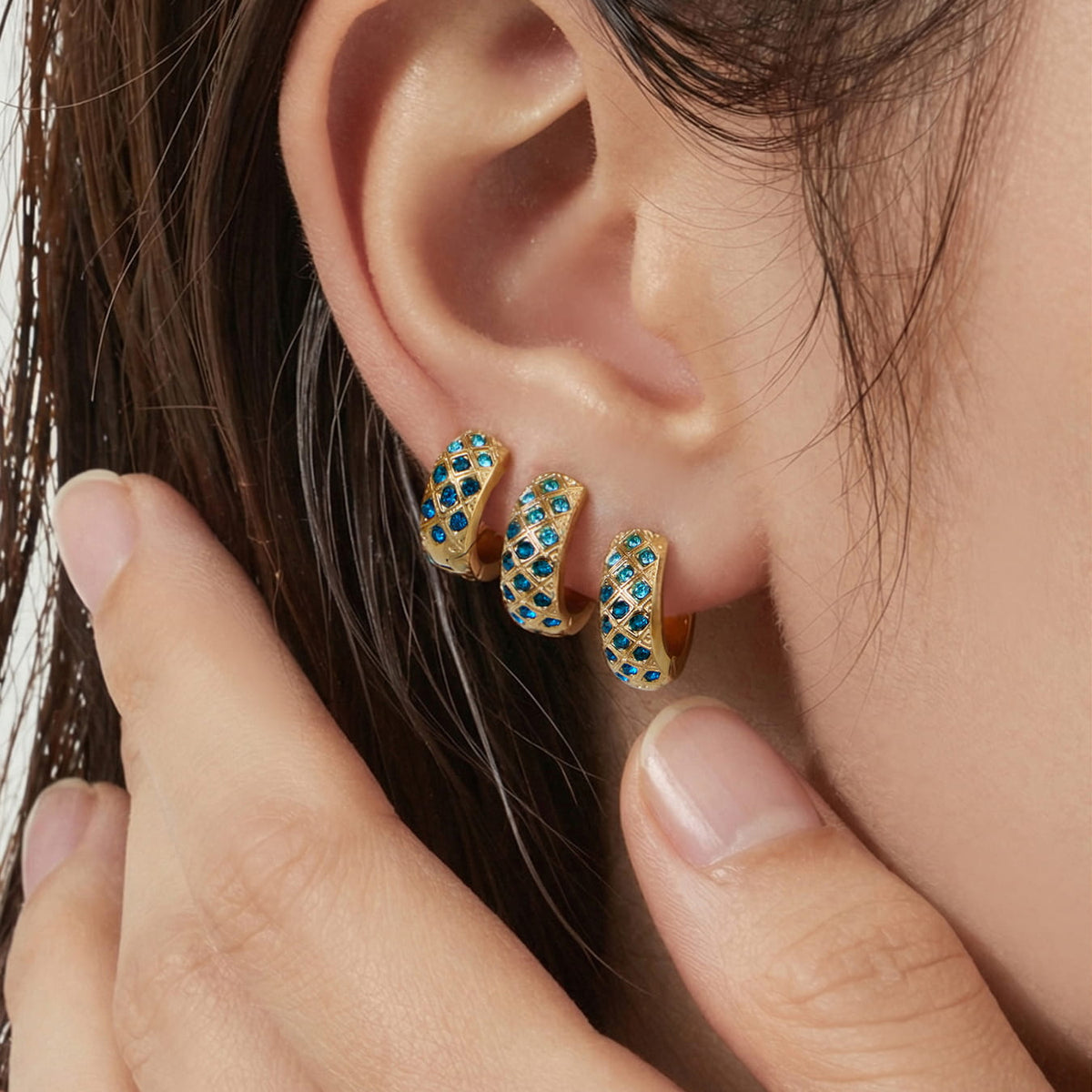 Three gold-tone blue CZ lattice hoop earrings shown at different sizes on an ear.