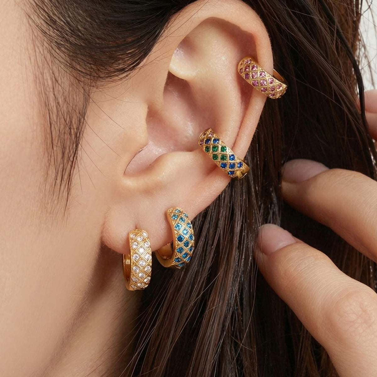 Gold-tone CZ lattice hoops with colorful stones worn in a layered ear stack.