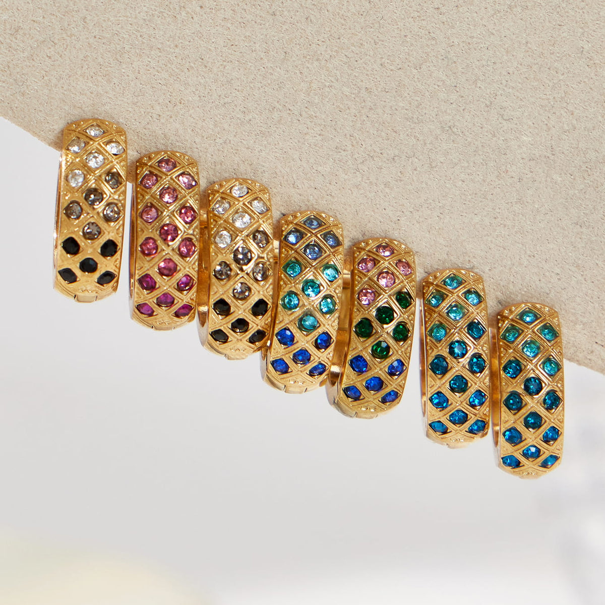 Gold-tone lattice hoop earrings with pink, blue, green and dark gradient CZ stones arranged on a stone block.