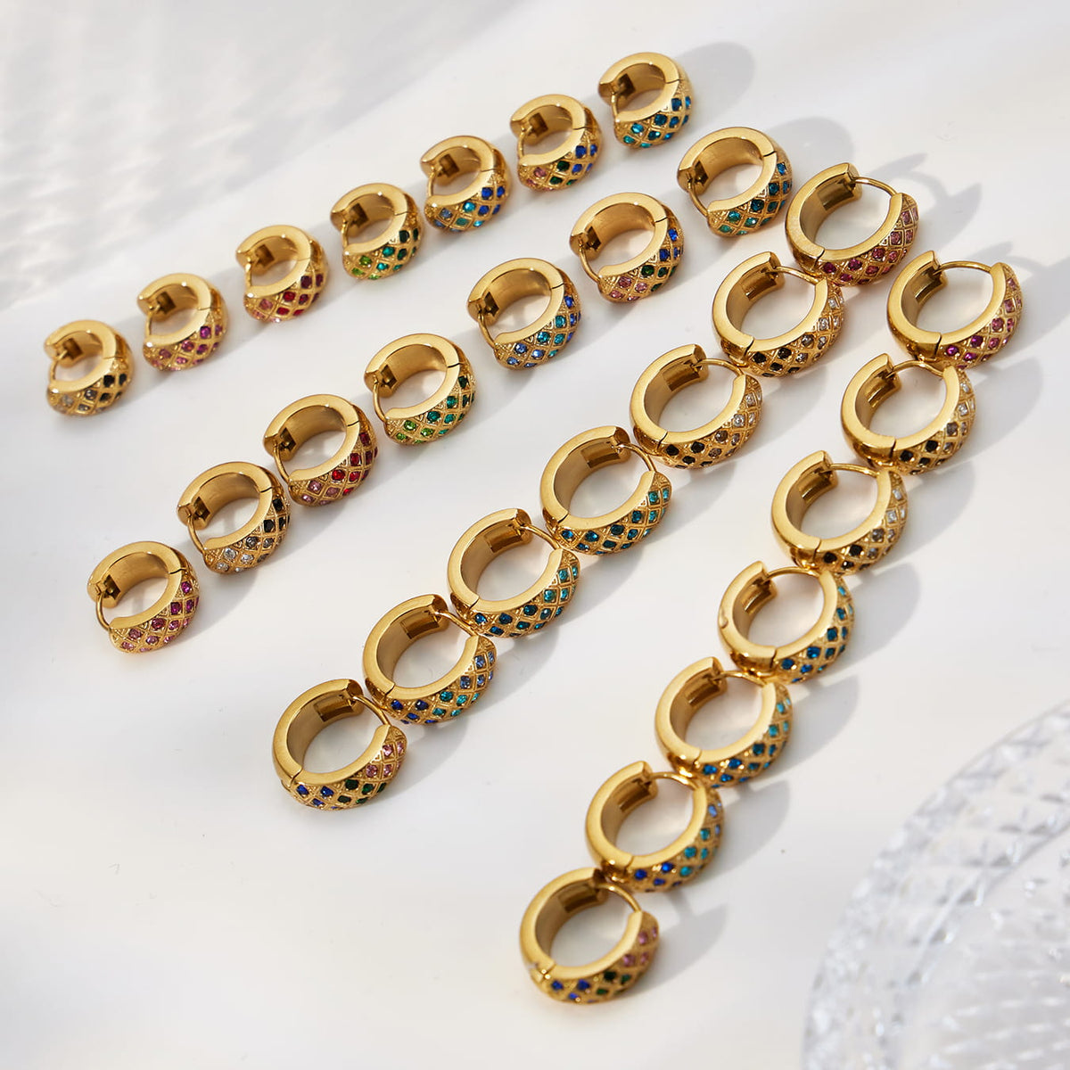 Gold-tone CZ lattice hoop earrings arranged by size and color with their hinged clasps visible.