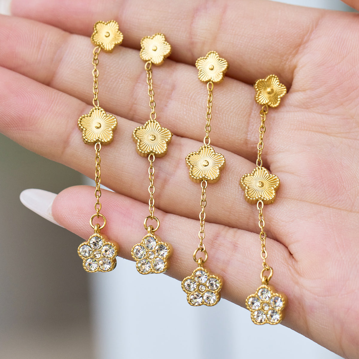 Hand display of gold flower drop earrings showing the layered floral design, chain links and zircon flower ends
