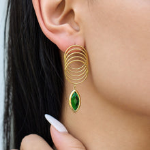 Model wearing green glass stone drop earrings with sculptural multi-loop stainless steel construction