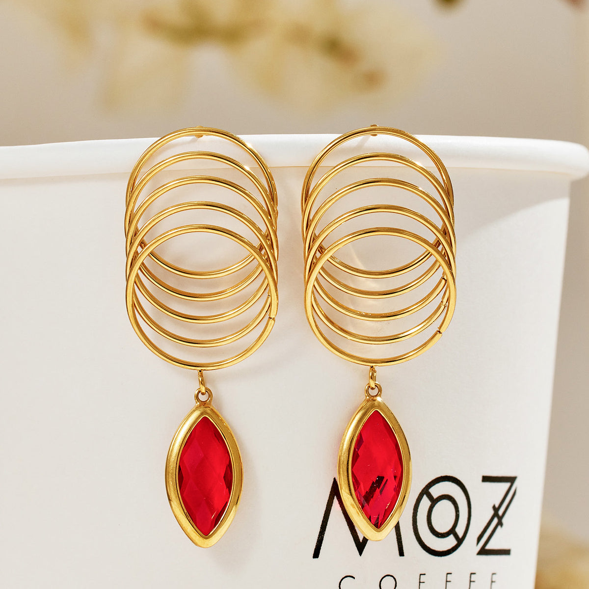 Pair of red faceted glass drop earrings with layered gold-tone loops displayed on a neutral jewelry background