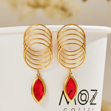 Pair of red faceted glass drop earrings with layered gold-tone loops displayed on a neutral jewelry background