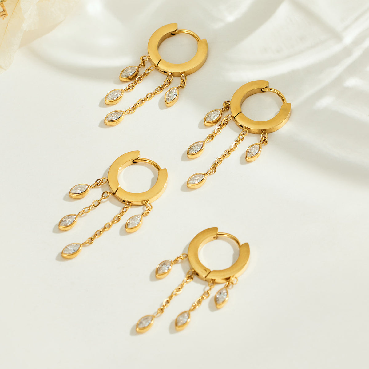 Multiple gold dangle hoop earrings displayed together with chain drops and marquise zircon charms for boutique selection