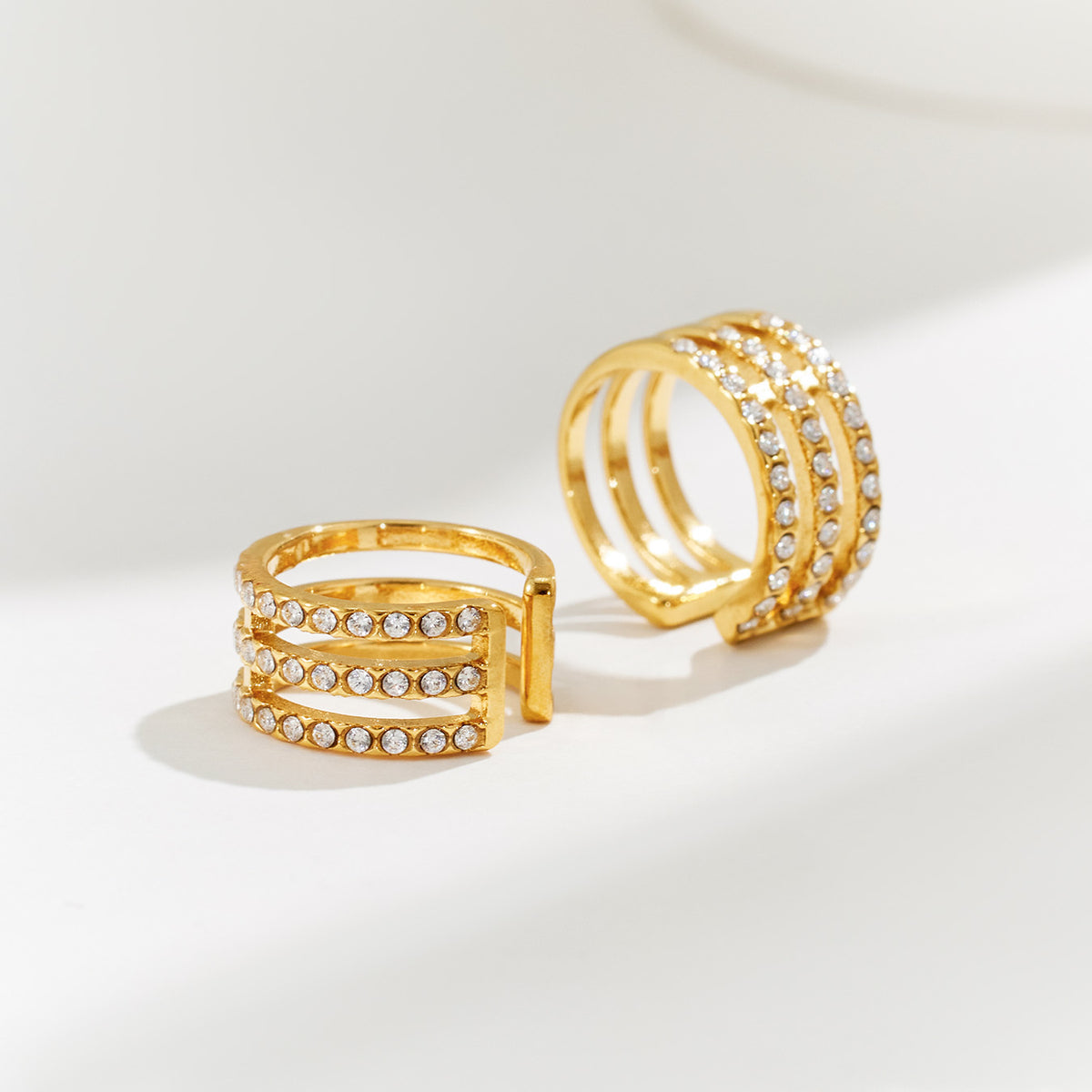 Pair of gold layered ear cuffs with multiple zircon-set rows displayed on a neutral jewelry surface