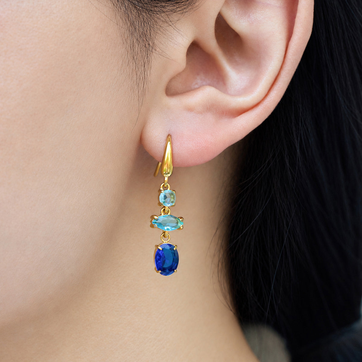 Gold-tone fishhook earring featuring turquoise-blue accents and a deep blue oval drop stone worn on a model's ear