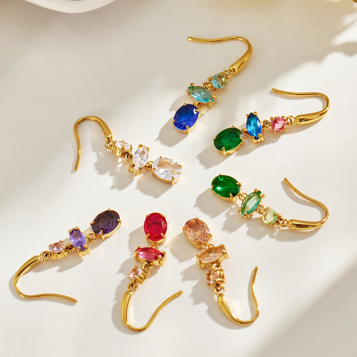 Flat lay of gold-tone stainless steel drop earrings with blue, red, green, purple, champagne and clear stones arranged on a light surface