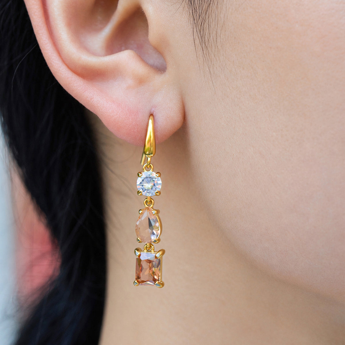 Close-up of a gold fishhook earring with three champagne and pale golden stones arranged vertically
