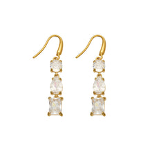 Pair of gold-tone stainless steel fishhook drop earrings with clear round, pear-shaped and rectangular stones on a white background