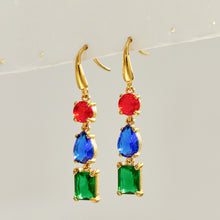 Pair of gold three-stone fishhook earrings featuring red round stones, blue pear-shaped stones and green rectangular drops