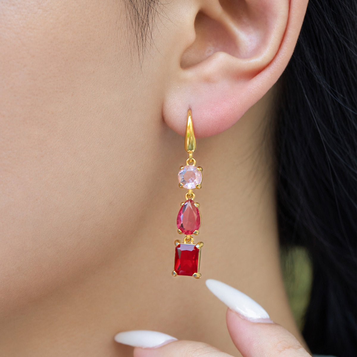 Gold fishhook drop earring with light pink and red faceted stones worn on a model's ear