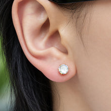 Close-up of a clear round stone stud earring set in polished gold-tone prongs on the earlobe