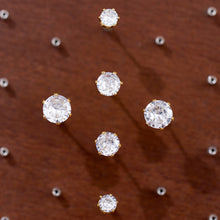 Several sparkling round clear stone studs displayed in different sizes on a brown textured background