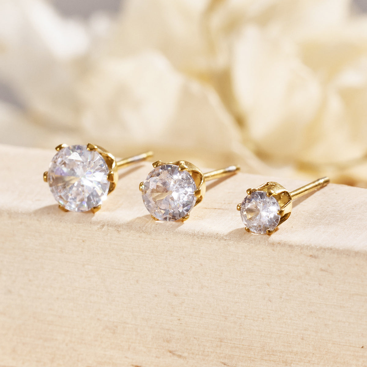 Round clear stone stud earrings with gold-tone prong settings displayed in a row on a neutral surface