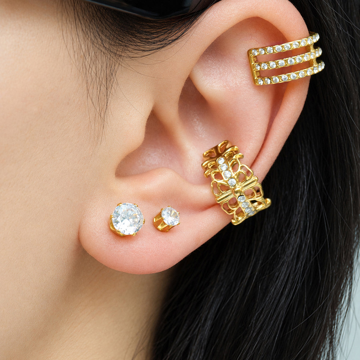 Close-up of gold-tone round stud earrings worn with layered gold ear jewelry on a model's ear