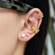 Model wearing a small round clear stone stud earring styled with multiple gold ear accessories