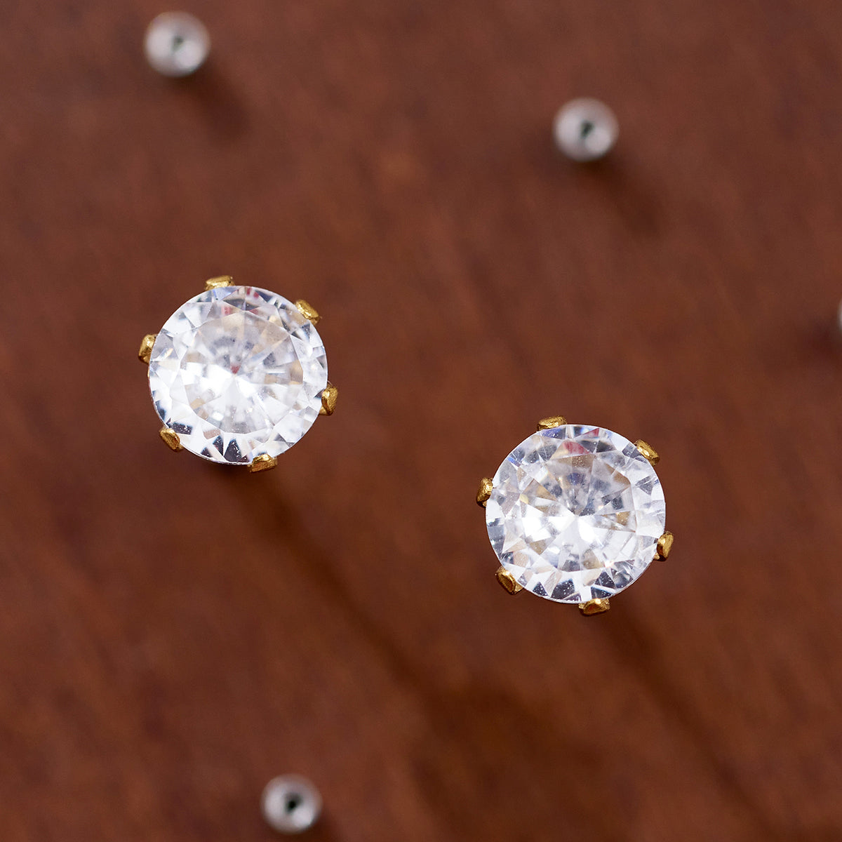 Two larger round clear stone stud earrings displayed on a brown surface, highlighting their faceted stone fronts