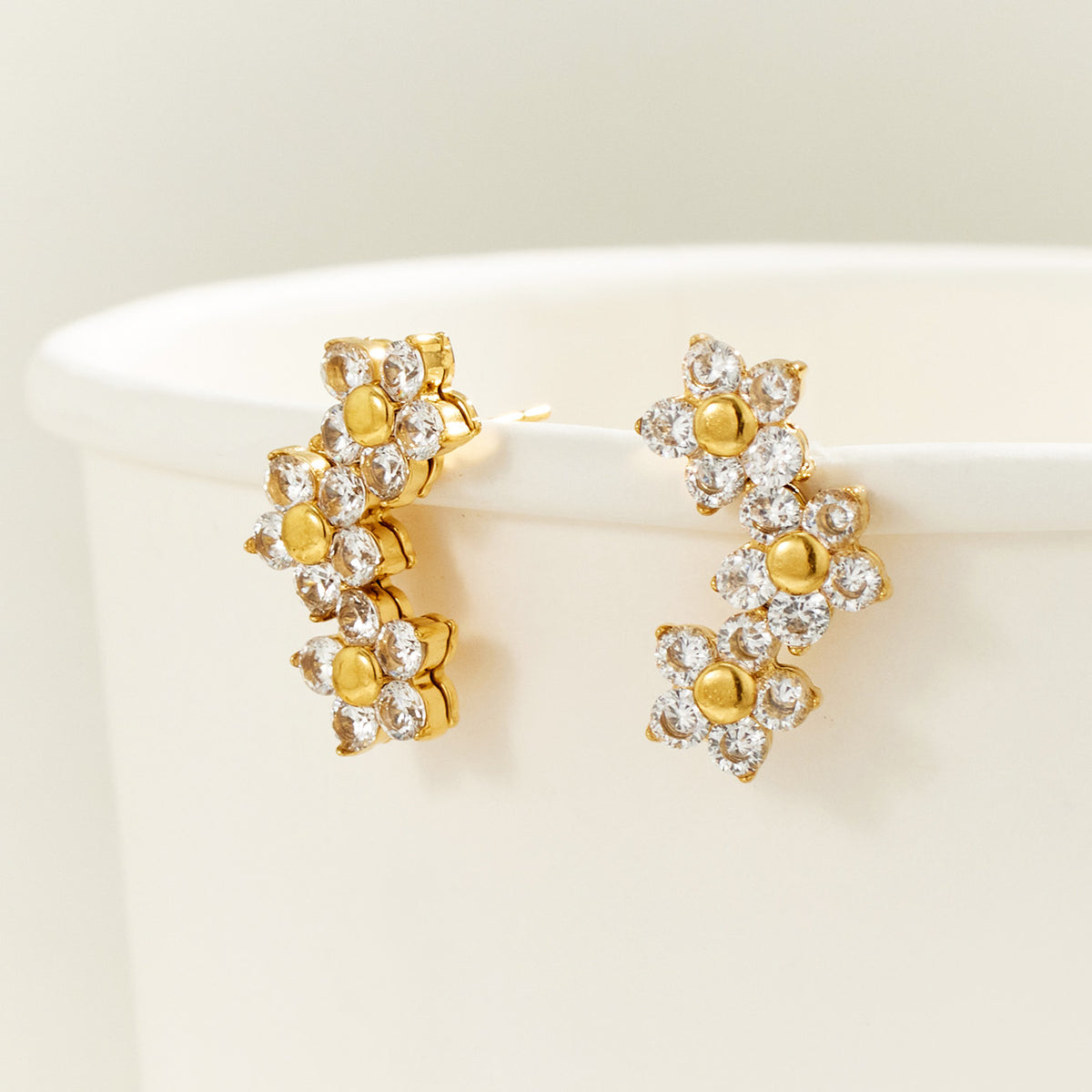 Gold-tone three-flower cluster earrings displayed upright on a cream surface, highlighting the cascading floral silhouette