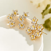 Gold-tone flower cluster earrings arranged on a light display surface, showing sparkling floral designs from different angles