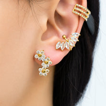 Model wearing gold three-flower cluster earrings with sparkling clear stones, styled alongside other gold ear jewelry