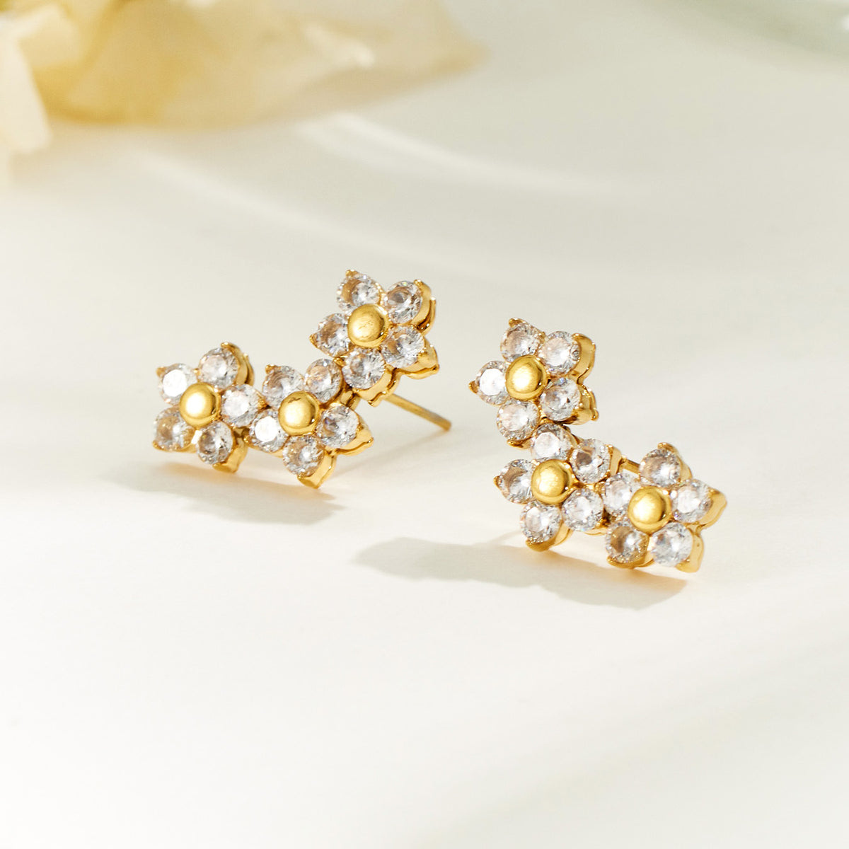 Pair of gold three-flower drop earrings displayed on a neutral surface with clear stone petals and round gold centers