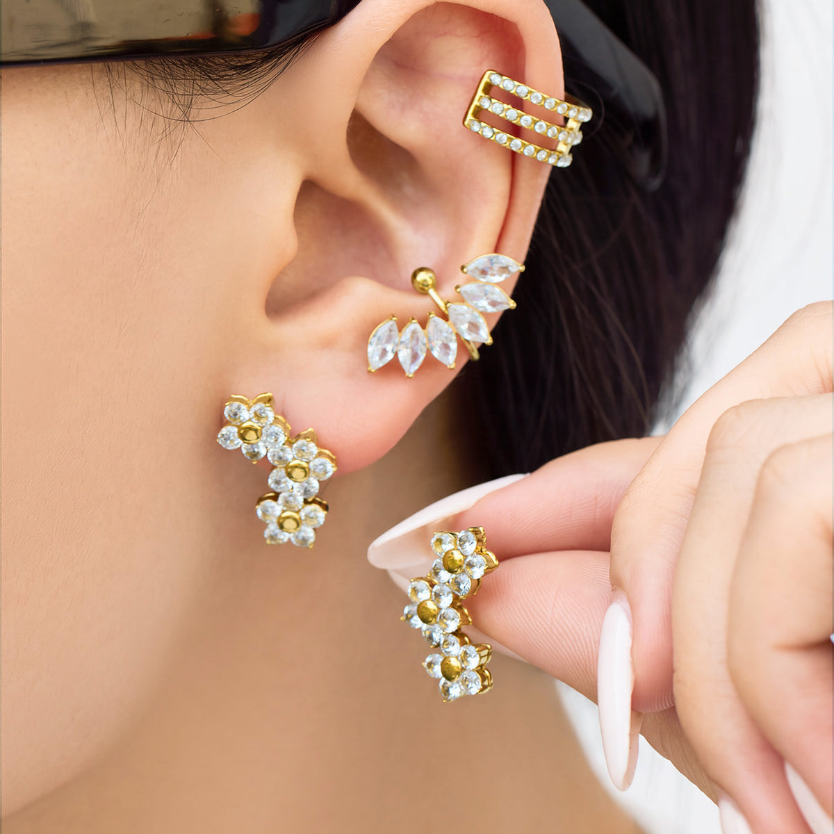 Close-up of a model wearing gold-tone three-flower earrings with clear stone petals and polished round centers