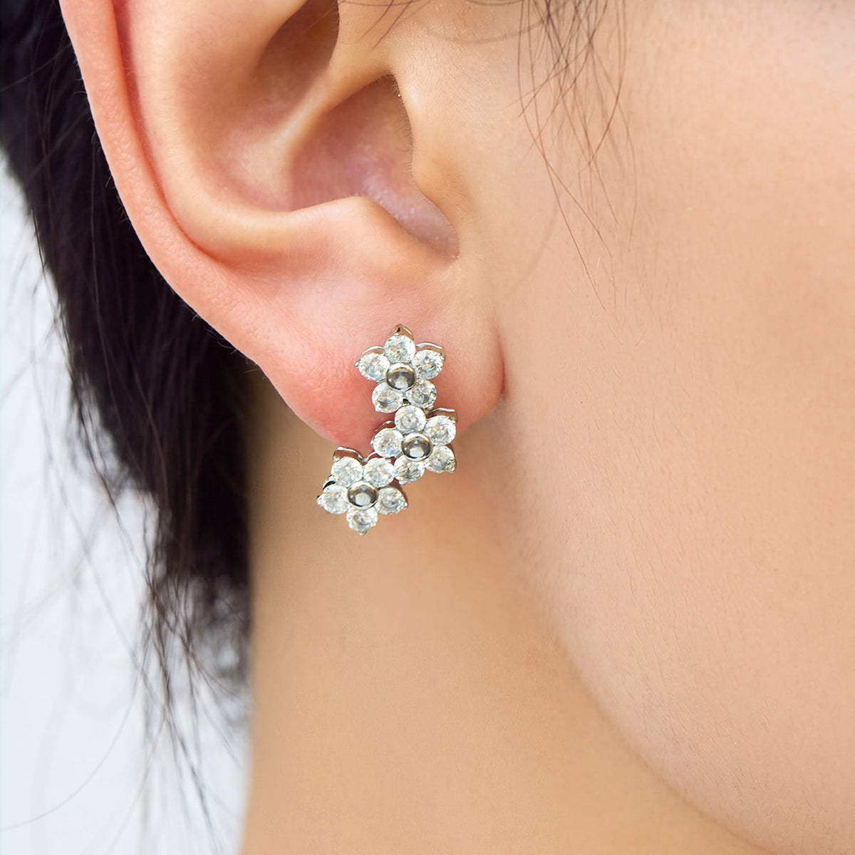 Silver-tone stainless steel three-flower cluster earring worn on a model's ear with clear faceted stone petals