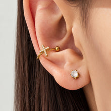 Gold-tone cross zircon ear cuff worn across the outer ear with a round clear stud earring.