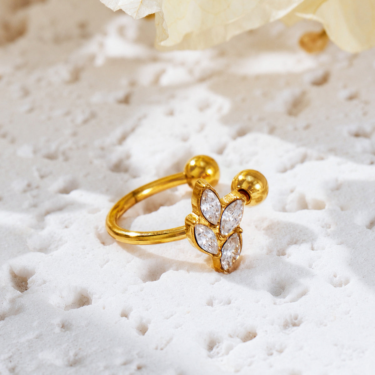 Gold-tone open ear cuff with four marquise-shaped clear stone details arranged like leaves on textured stone.