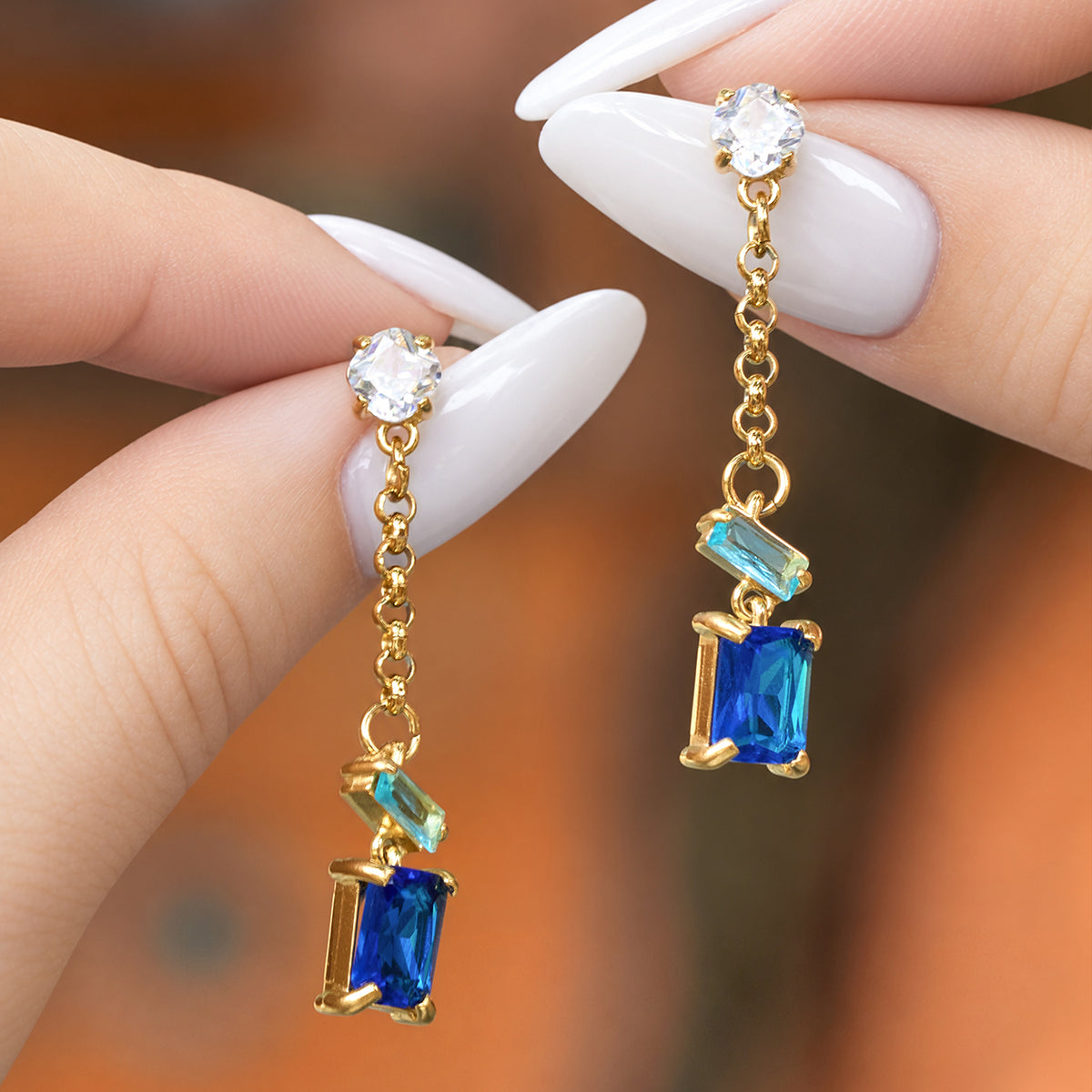 Hand-held blue baguette zircon drop earrings showing the clear top stone, gold links and rectangular blue stone