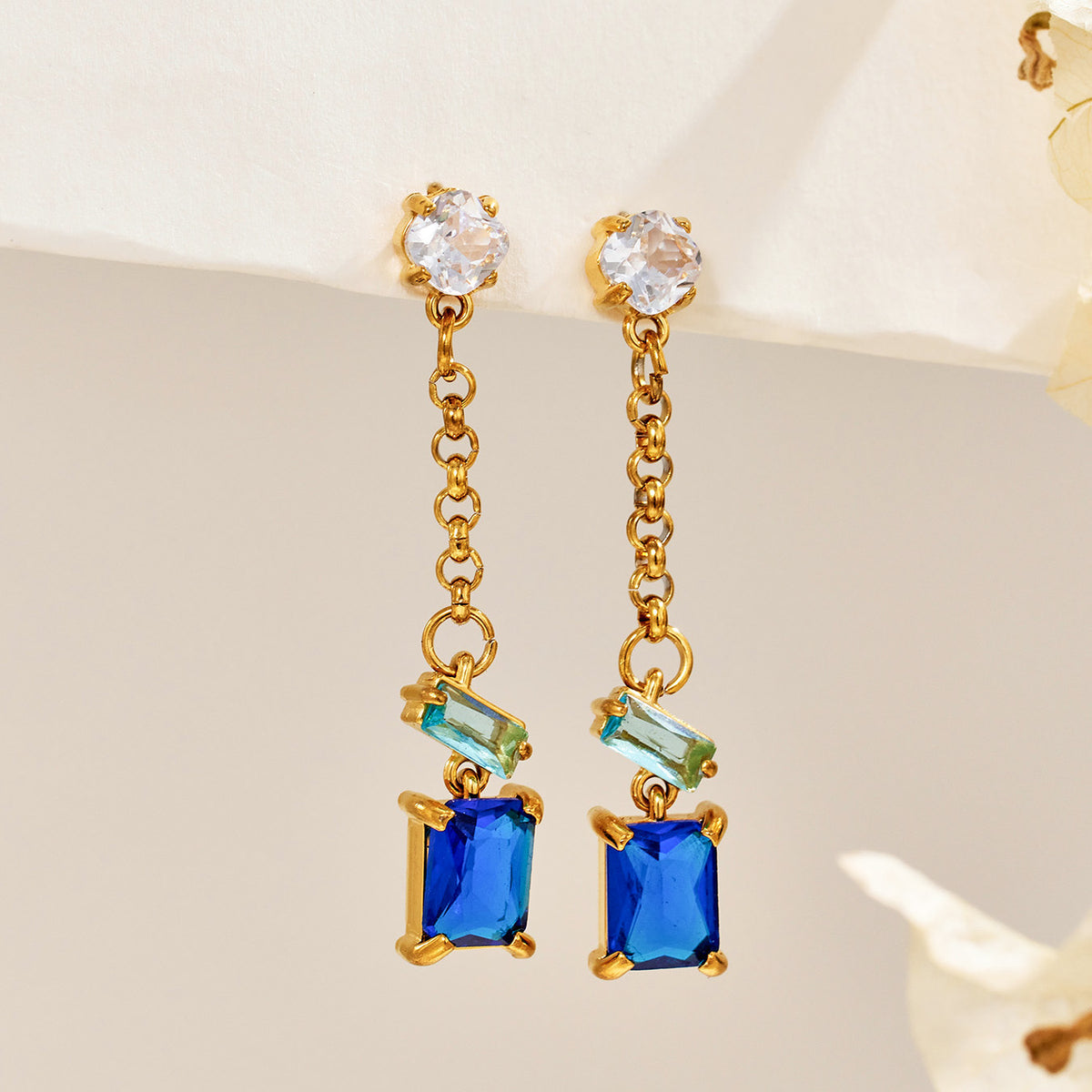 Blue zircon drop earrings photographed on a neutral background with geometric gold links and clear top stones