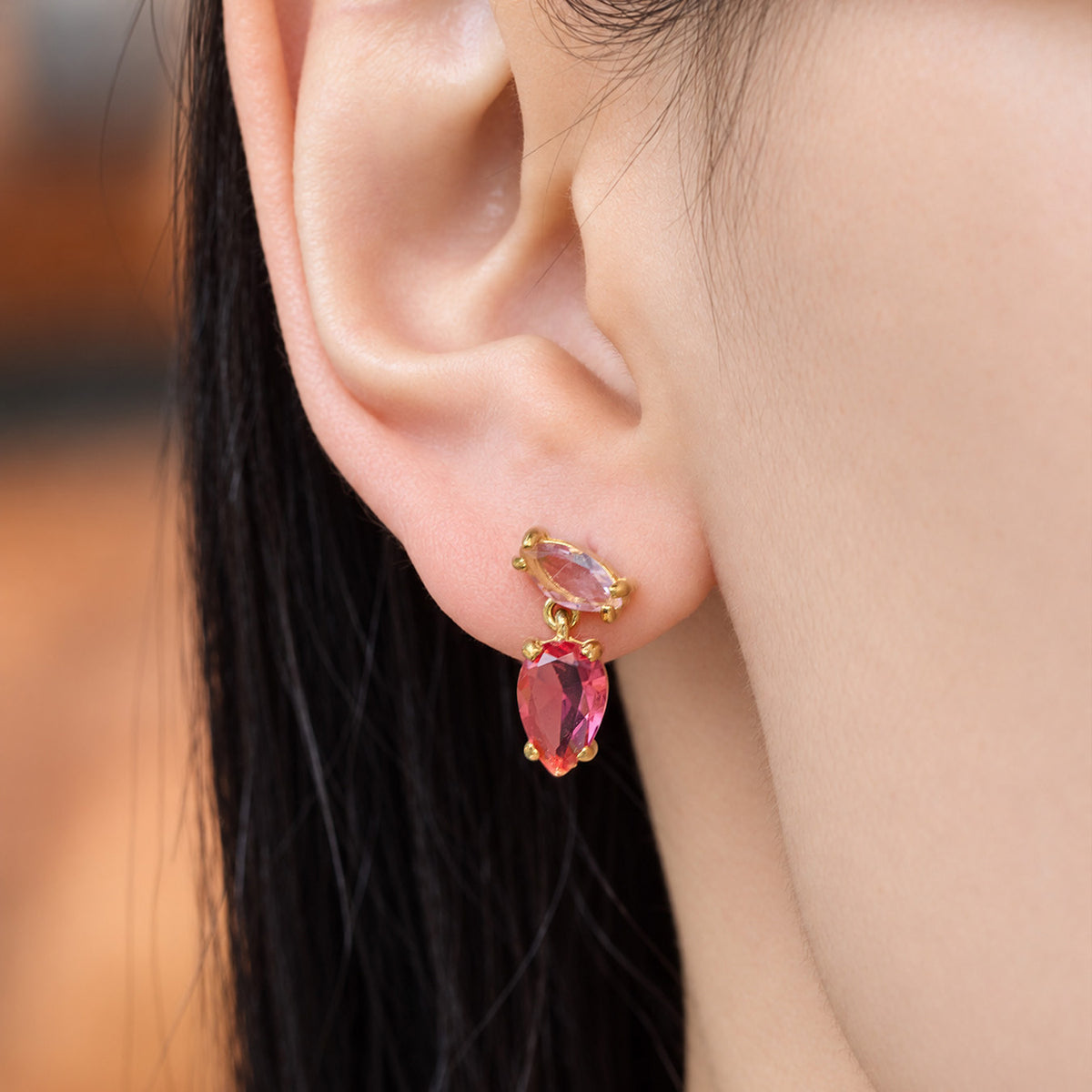 Close-up of red teardrop zircon earrings worn on the ear with a pink marquise top stone and gold-tone setting